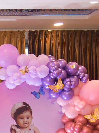 A personalized backdrop for a butterfly-themed party, featuring the birthday girl's photo. The design is framed by a lovely balloon garland in shades of pink and purple.