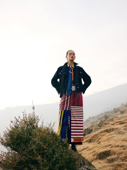 A powerful, heroic pose against the sky. The styling here is about strength and confidence, with the model standing tall in her environment.