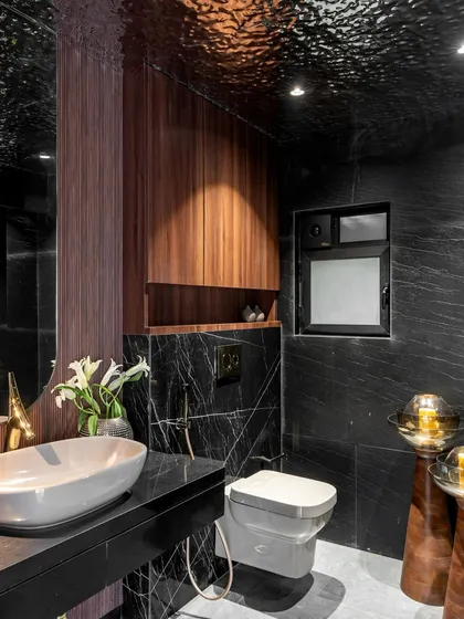 This powder room uses dark, moody tones to create a dramatic effect. The textured ceiling, black marble walls, and warm wood cabinetry combine to form a space that is both intimate and luxurious.
