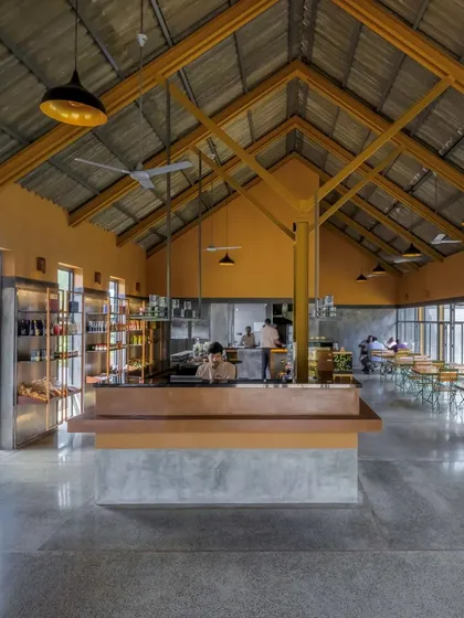 Inside the Teyla tea cafe in Kerala, we created a large, open volume with an exposed ISMB steel structure and a high, sloping roof. This design maximizes space and light, while the central open kitchen fosters a connection between the chefs and guests, reminiscent of a traditional local 'chaithela'.