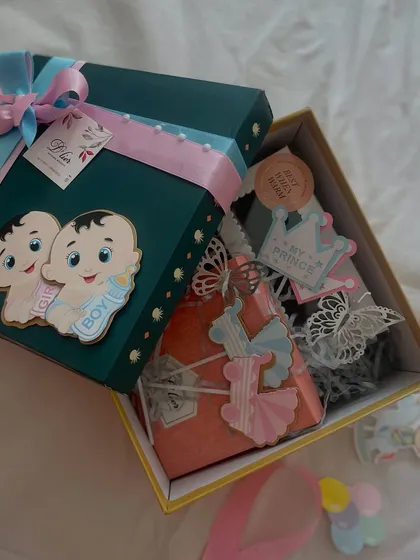 A special gift box curated for a mom-to-be, celebrating the upcoming arrival of a baby boy and girl. The box is adorned with pink and blue ribbons and cute baby-themed decorations.