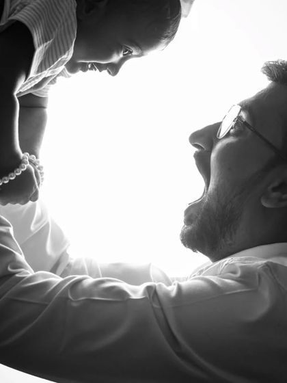 A joyful black and white backlit shot of a father and his child. The high-contrast lighting captures a moment of pure, uninhibited happiness.