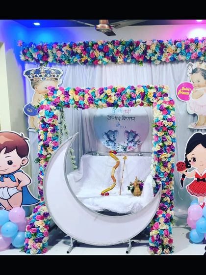 A colorful baby shower decoration with a floral swing and lighted moon. The setup is adorned with various cute cartoon character cutouts.