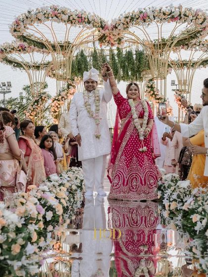 A joyous shot of the couple on the mirrored aisle, with their reflection creating a beautiful visual effect, framed by the floral decor.