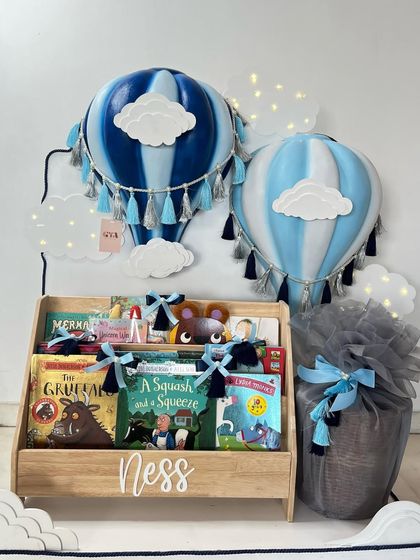 This personalized 'Ness' bookshelf is paired with blue and white hot air balloon lamps, creating a dreamy corner for story time.