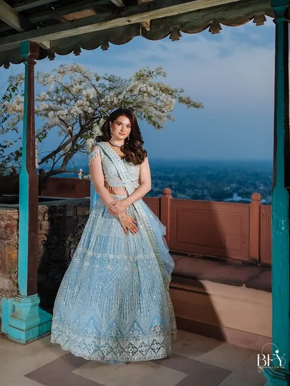 A full-length portrait of a bride in her powder blue lehenga, posing on a balcony at dusk.