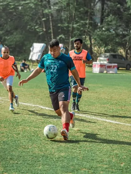 A player dribbles the ball forward during a corporate match, navigating the pitch with skill and agility.