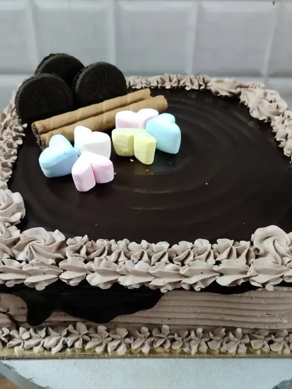 A square chocolate cake topped with Oreos, wafer rolls, and colorful heart-shaped marshmallows.