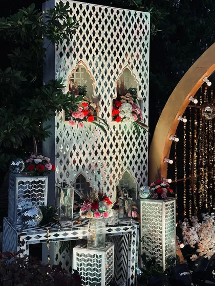 A detailed view of the Sangeet decor, showing white latticework panels with floral arrangements in the niches, placed next to the shimmering entrance tunnel.