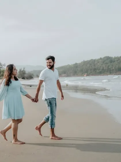 A full-length shot of the couple walking hand-in-hand, showcasing the beautiful expanse of the beach and sea.