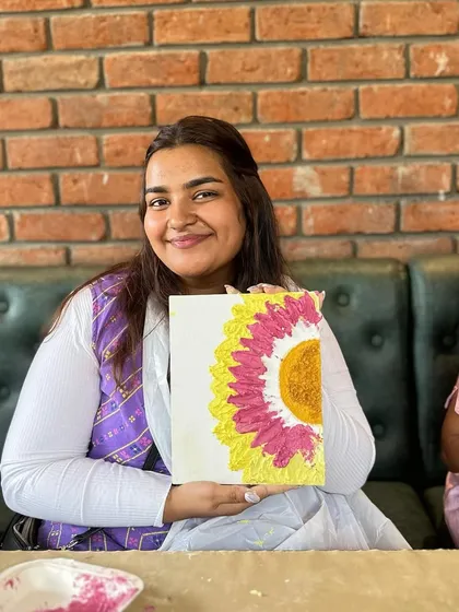A participant smiling with her completed sunflower texture painting. The joy of creating something with your own hands is unmatched.
