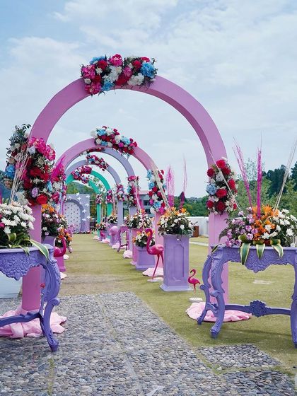 A carnival-themed Mehendi entrance with a rainbow of pastel arches. Each arch is topped with colorful floral arrangements, and the aisle is lined with vintage-style consoles, creating a vibrant and festive welcome.