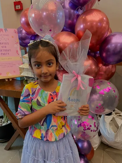 This sweet girl is holding her personalized return gift against a backdrop of festive balloons. Her smile says it all!