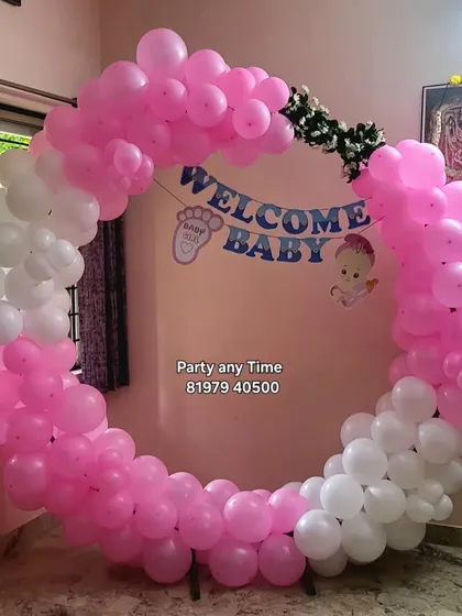 A simple 'Welcome Baby' decoration with a pink and white circular balloon arch, perfect for a baby girl's naming ceremony or welcome home party.