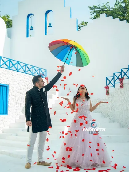 A joyful and colorful moment captured at a Santorini-themed set. The rainbow umbrella and shower of rose petals add a touch of whimsy and romance.