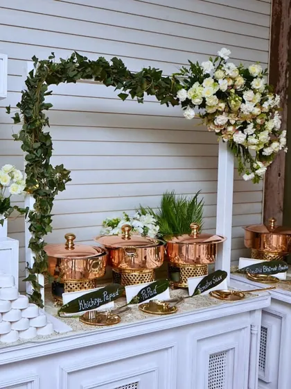 A traditional buffet setup featuring gleaming copper serving dishes on a white counter. The combination of classic materials and fresh floral decor creates a timeless look.