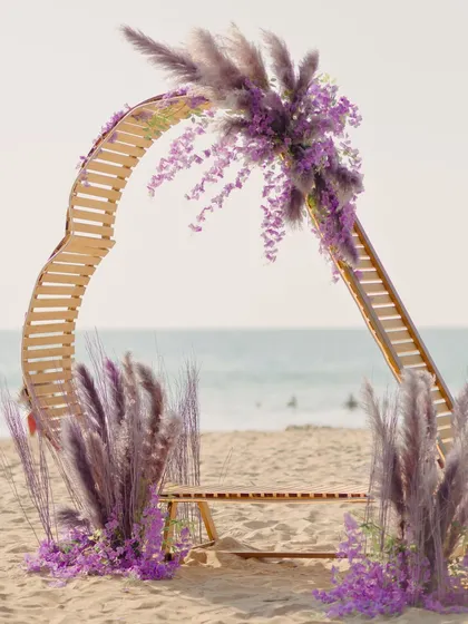 A unique, sculptural photo booth designed for the beach. The curved wooden arch, adorned with lilac pampas grass and florals, provided a stunning, on-theme backdrop against the sea.