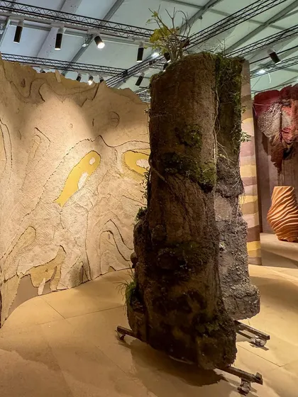 An overview of the 'Soil' installation, where structures resembling ancient earth cores stand beside a wall depicting a topographical map. The piece fuses modern technology with handcrafted craftsmanship.
