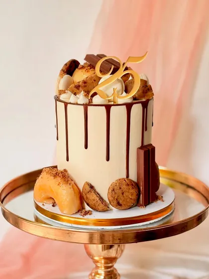 My signature modern drip cake, perfect for a milestone 25th birthday. This tall cake has a smooth buttercream finish, a rich chocolate drip, and is generously topped with donuts, cookies, and chocolate bars.