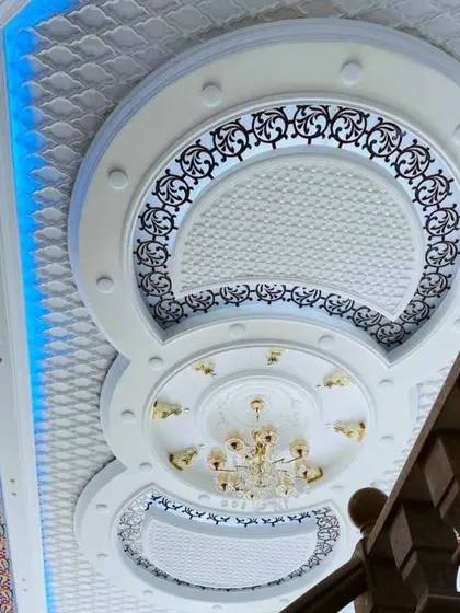 A magnificent, multi-layered circular ceiling with intricate patterns and a grand chandelier. The blue accent lighting along the side adds a modern touch to a classic design.