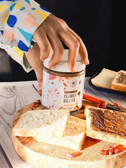 A lifestyle shot showing a hand reaching for the jar of YB Peanut Butter, adding a human touch and making the product feel more accessible.