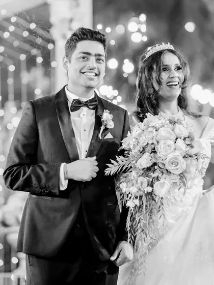 A candid black and white shot of Alice and Avi's grand entrance. The image captures their high energy and happiness as they walk in, surrounded by lights and cold pyrotechnics.