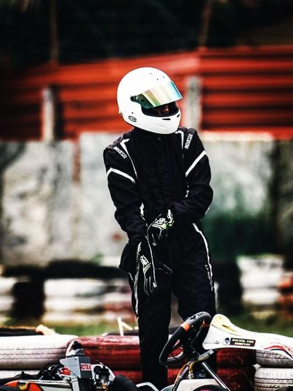 A driver standing by his kart in the pit area.
