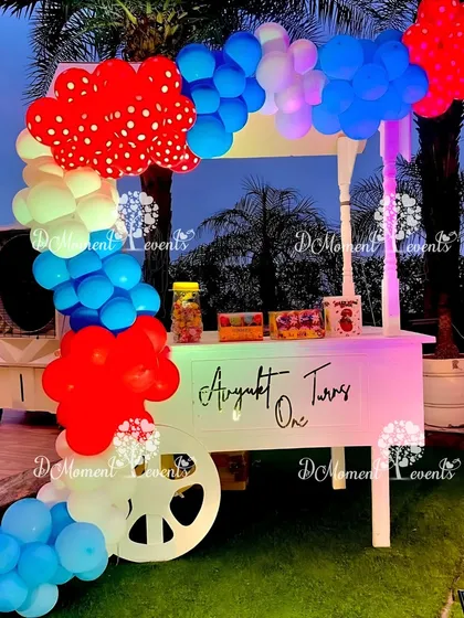 A charming candy cart for an outdoor carnival party. The cart is decorated with a red, white, and blue balloon arch and is ready to be filled with treats for the guests.
