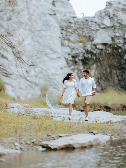 A couple walks hand-in-hand along the edge of a quarry lake. The wide shot emphasizes the beautiful, rugged landscape surrounding them.