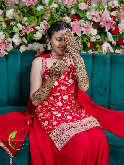 A happy bride posing against a beautiful floral backdrop, her intricate mehendi design adding to her overall look.