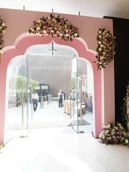 A custom designed entrance for the wedding ceremony, featuring a scalloped arch in soft pink, adorned with floral arrangements.
