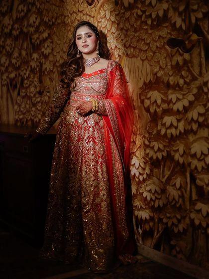 A full-length portrait of the bride against an ornate, textured wall. Her red and gold outfit looks regal and timeless.