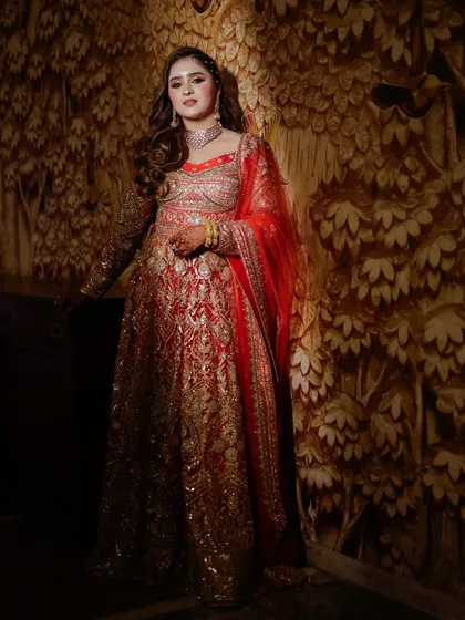 A full-length portrait of the bride against an ornate, textured wall. Her red and gold outfit looks regal and timeless.