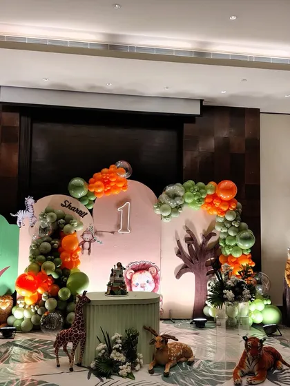 A full view of a "Wild One" first birthday setup. The decor features a large number '1', a custom name sign, and a variety of plush and model jungle animals set against a backdrop of organic balloon garlands and tree cutouts.