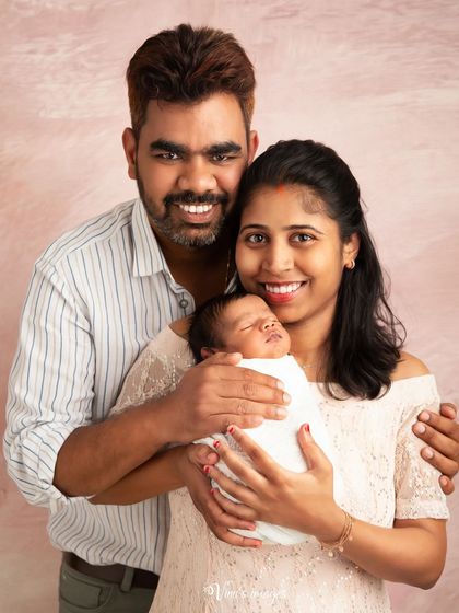 A classic first family portrait. This image showcases the happy new parents with their sleeping newborn, a timeless keepsake to announce their little one to the world.