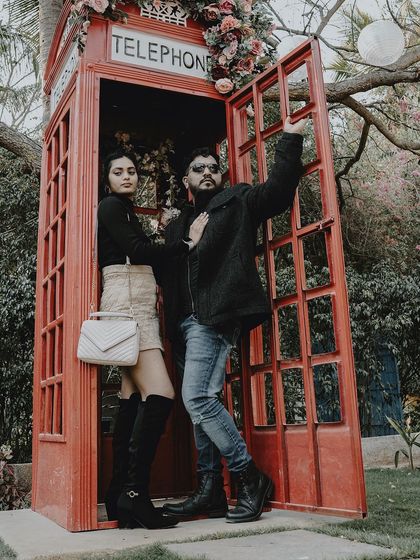 A cool, high-fashion pose in a red telephone booth, with the couple showing off their stylish winter outfits.