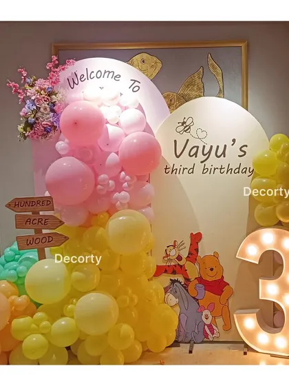 A classic Winnie the Pooh theme for Vayu's third birthday. The setup includes a welcome sign, character cutouts, and a large light-up number three.