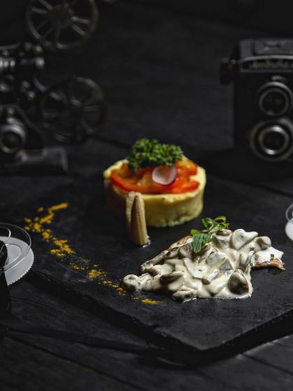 A deconstructed dish of creamy sautéed mushrooms served alongside a turmeric mashed rice salad. The vintage camera props in the background hint at our cinematic and artful approach to food styling.