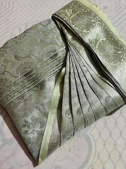 A light green Banarasi silk saree with intricate silver work, folded to showcase its beauty while keeping it safe.