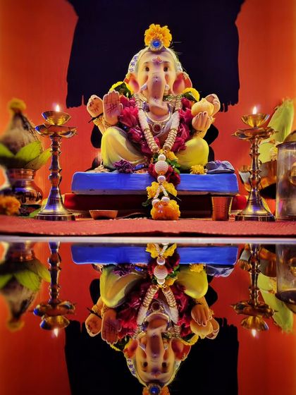 An artistic reflection shot of a Ganesh idol. The perfect symmetry and the colorful top half mirrored against the table surface create a visually striking image.