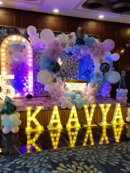 A full stage setup for a Frozen party, featuring a circular balloon arch, sequin backdrop, and large marquee letters.
