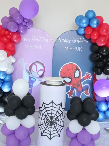 A joint Spider-Man themed birthday for twins. The setup features two separate arched backdrops for each child, with colorful balloon arrangements and a spider-web-themed plinth in the center.