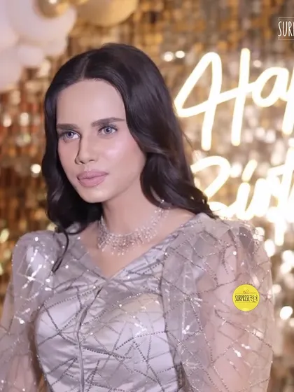 A guest at a birthday party we styled. The backdrop features a "Happy Birthday" neon sign and a sophisticated gold and white balloon arrangement, creating an elegant and glamorous atmosphere.