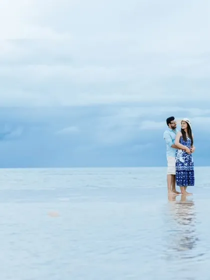 A romantic embrace in the tranquil sea during a beach pre-wedding session. The soft blue and grey tones of the water and sky give this photo a dreamy quality.