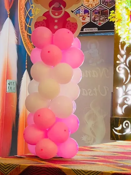 A simple yet elegant balloon pillar in shades of pink, part of a larger Naming Ceremony decoration in a banquet hall.