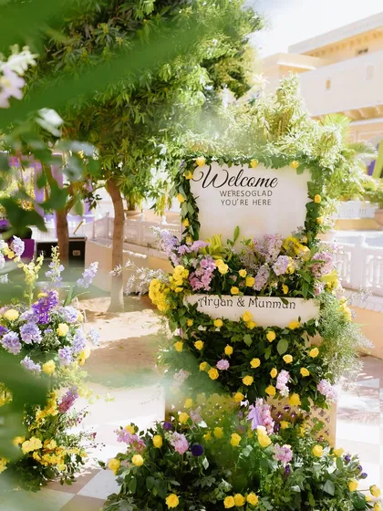 The beautiful welcome sign for the Haldi ceremony, enveloped in a cascade of fresh yellow and lavender flowers, setting a warm and inviting tone for guests.