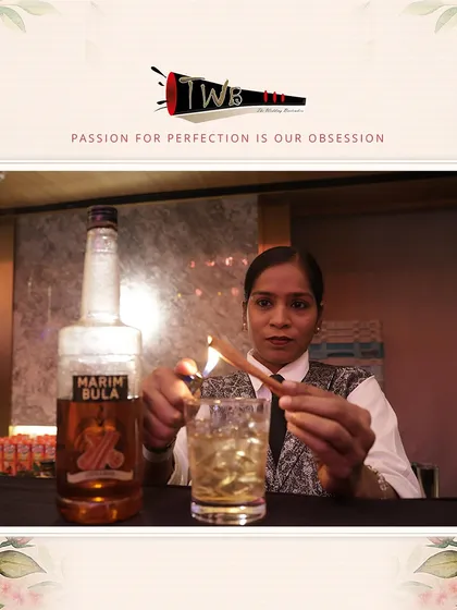 A female bartender expertly smokes a cinnamon stick to garnish a cocktail, adding a warm, spicy aroma to the drink.