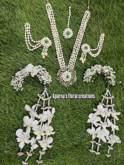 An elegant all-white floral jewellery set featuring delicate orchids. The set includes a necklace, earrings, maang tikka, and bajuband with cascading flowers.