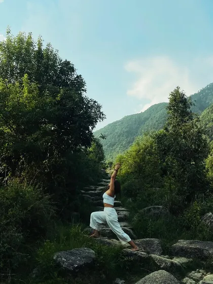 Reaching for the sky in a warrior pose amidst the Himalayan greenery. Practicing yoga outdoors allows us to draw energy directly from the earth and the vastness of nature.