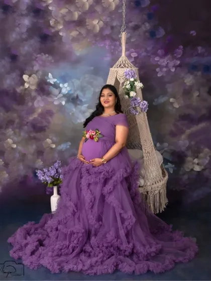 The full length of the magnificent purple gown is on display in this shot, creating a stunning visual as she sits gracefully on the floral swing.